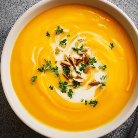 Cremige, geröstete Kürbissuppe mit frischen Kräutern und knusprigem Brot serviert.